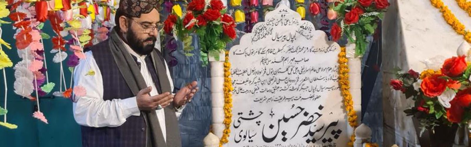 A visitor raising his hands in dua beside a flower-decorated shrine