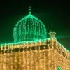 A green-domed shrine illuminated at night during an Islamic commemoration