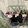 Community members seated under a marquee during a large outdoor gathering